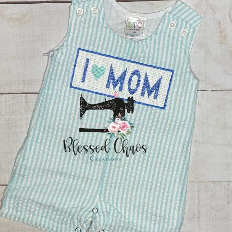 May include: A light blue and white striped baby onesie with a blue and white embroidered patch that says "I love Mom" with a heart. Below the patch is a black and white sewing machine with pink flowers. The onesie has a white text that says "Blessed Chaos Creations".