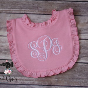May include: Pink baby bib with a white ruffled edge and a white embroidered monogram "SPS".