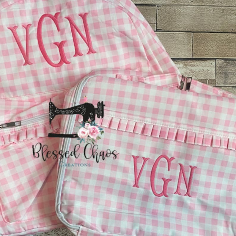May include: Pink and white gingham backpack and lunch bag with the monogram "VGN" embroidered on both. The lunch bag has a ruffled trim and the text "Blessed Chaos Creations" is printed on the front.