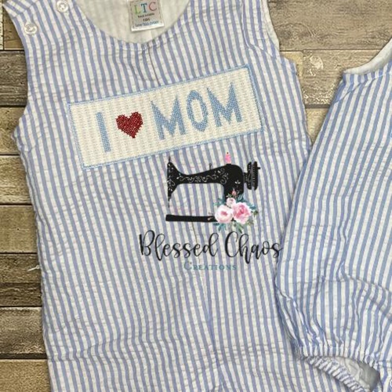 May include: A blue and white striped baby onesie with a white embroidered patch that says "I love Mom" with a red heart. The onesie is made by Blessed Chaos Creations.