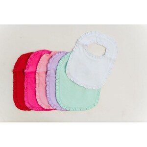 May include: Set of seven baby bibs with ruffled edges in various colors, including red, pink, light pink, lavender, light green, and white.