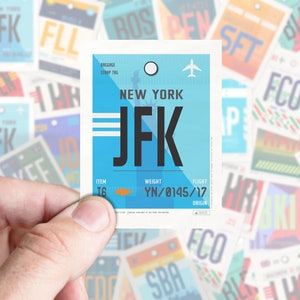 Op de afbeelding: Een blauwe en witte bagagelabel met de tekst "NEW YORK JFK" en de vluchtinformatie "YN/0145/17".