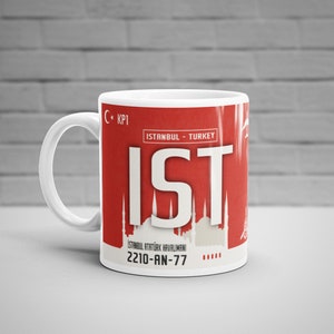 Może przedstawiać: Biały kubek ceramiczny z czerwonym wzorem przedstawiającym tekst "IST" i "ISTANBUL - TURKEY". Kubek zawiera również tekst "C+ KPI" i "2210-AN-77".