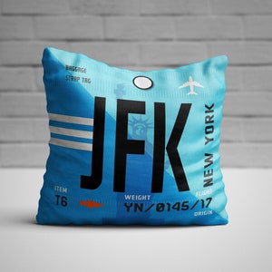 May include: Blue and white throw pillow with a luggage tag design featuring the text "JFK NEW YORK" and the words "ITEM T6", "WEIGHT YN/0145/17", and "FLIGHT ORIGIN".