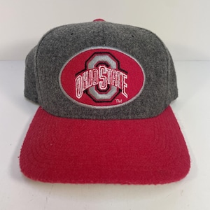 Könnte beinhalten: Graue und rote Baseballkappe mit dem Ohio State-Logo. Die Kappe hat einen roten Schirm und eine graue Krone. Das Ohio State-Logo befindet sich in einem roten Oval mit weißen und grauen Buchstaben.