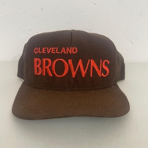 Op de afbeelding: Bruine baseballcap met de tekst "CLEVELAND BROWNS" in oranje geborduurd. De cap heeft een gebogen klep en een gestructureerde kroon, voor sportliefhebbers.