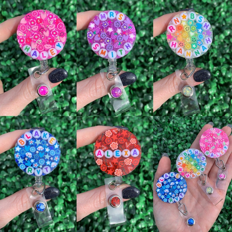 May include: Six colorful, round, personalized name badges with glitter and colorful beads. Each badge has a different name, including Haley, Mrs. Smith, Hannah, Blake, Alexa, and a second Hannah badge. The badges are attached to clear retractable badge holders.
