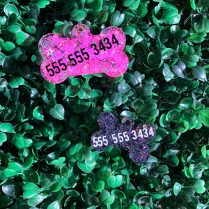 May include: Two dog bone-shaped pet tags with contact information. One tag is pink with glitter and the phone number 555 555 3434. The other tag is dark blue with glitter and the same phone number.