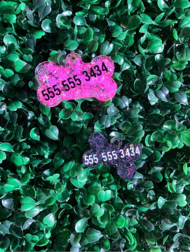 May include: Two dog bone-shaped pet tags with contact information. One tag is pink with glitter and the phone number 555 555 3434. The other tag is dark blue with glitter and the same phone number.