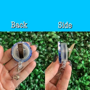 May include: A blue and white glitter retractable badge holder with a gold clip. The back of the holder shows the clip and the front shows the glitter.