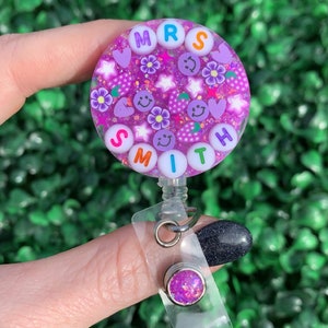 May include: Purple glitter badge holder with the name "MRS SMITH" spelled out in colorful letters. The badge holder has a clear plastic strap and a small purple glitter charm.