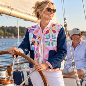 May include: A long-sleeve jacket featuring a quilted front panel with a colorful geometric star pattern in shades of pink, yellow, and blue, contrasted by solid dark blue sleeves and back panels, finished with a light pink trim and gold buttons.