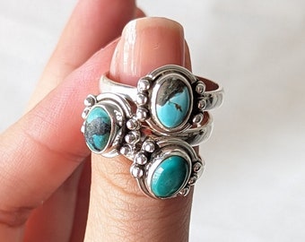 Peut inclure: Trois bagues en argent avec des pierres ovales turquoise sont empilées sur un doigt. Les bagues ont un design détaillé autour des pierres. Le fond est de couleur blanc cassé. La personne porte un pull rouille.