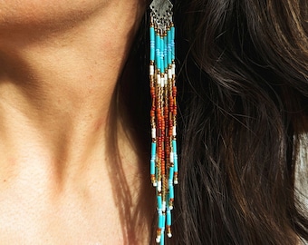 May include: A pair of long, turquoise, white, gold, and orange beaded earrings with a silver charm at the top.