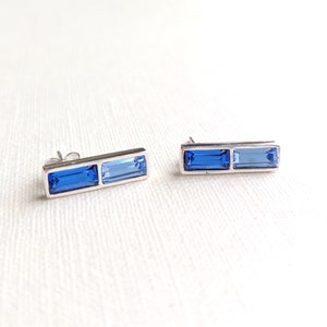 May include: A pair of silver earrings with two blue rectangular gemstones. The earrings are simple and elegant.