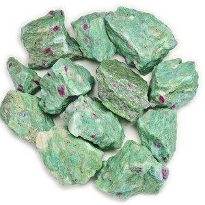 Pode incluir: Uma coleção de pedras brutas de zoisita rubi verdes e vermelhas. As pedras têm uma forma irregular e uma textura áspera e natural.