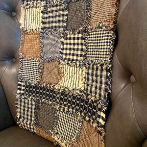 May include: A patchwork quilt throw pillow with a frayed edge, featuring a variety of black, brown, and cream plaid patterns.