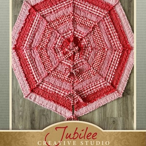 May include: Red and pink gingham Christmas tree skirt with a ruffled edge. The skirt is made of fabric scraps and has a patchwork design. The text "Tis the Season Christmas Tree Skirt Pattern" is printed on the bottom of the image.