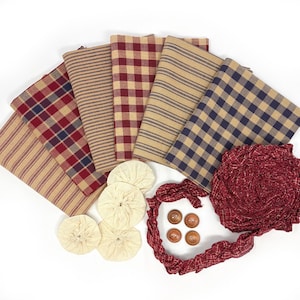 May include: A collection of fabric pieces in various patterns, including stripes and plaid, in shades of tan, red, and navy. Also included are cream-colored fabric circles, wooden buttons, and a red fabric rope, all arranged on a white surface.