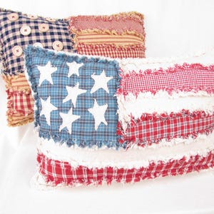 May include: Two decorative pillows featuring a patchwork American flag design. The pillows are made of red, white, and blue fabric with a frayed edge. One pillow has a blue background with white stars and the other has red and white checkered fabric.