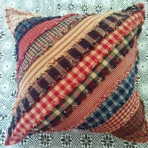 Peut inclure: Un oreiller patchwork rouge, blanc et bleu avec des bords effilochés. L'oreiller est fait de différents tissus à carreaux et à carreaux.