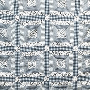 May include: A quilt made of blue and white fabric with a geometric pattern. The quilt is made of squares and rectangles, and the fabric is a mix of stripes, checks, and floral prints.
