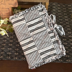 May include: A black and white striped quilted book cover with frayed edges and a bow. The cover is made of fabric and has a patchwork design.