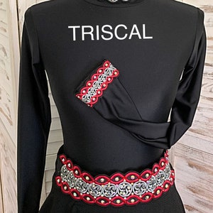 May include: Black long-sleeved dress with silver and red decorative trim. The trim is featured on the neckline, sleeve, and waist. The word "TRISCAL" is printed in white on the dress.