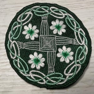 May include: A green and white embroidered patch featuring a Celtic cross with four shamrocks around it. The cross is surrounded by a Celtic knot design.