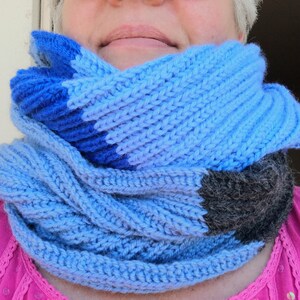 Pode incluir: Uma echarpe infinita de malha azul e cinza com um design trançado. A echarpe é feita de fio macio e é perfeita para se manter aquecido no inverno.