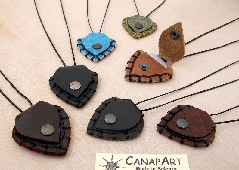 May include: Seven leather necklaces with a variety of colors and designs. Each necklace features a small, heart-shaped pendant with a metal button closure. The pendants are made of leather and have a stitched edge.