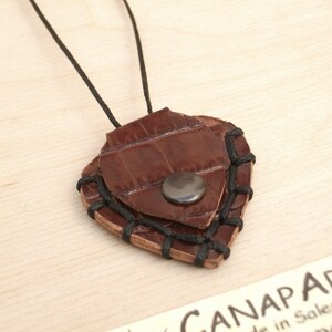 May include: A brown leather guitar pick necklace with black stitching and a silver button. The pick is shaped like a heart.