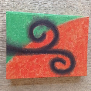 May include: A handmade journal with a textured cover featuring a black abstract design on a green and orange background.