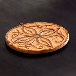 May include: A round wooden ornament with a carved floral design. The ornament is light brown in color and has a copper-colored wire loop for hanging.