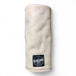 May include: Cream-colored golf club head cover. The cover is made of a soft, textured material. A black rectangular patch at the bottom features the text "REINLAND Golf Co" and a crossed golf club design.