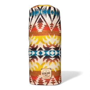 May include: A cylindrical golf club head cover with a Southwestern geometric pattern in shades of cream, brown, yellow, orange, and teal. The cover has a small rectangular tag with the text "REINLAND" and a logo.