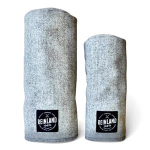 May include: Two gray felt golf club covers. The covers are cylindrical and have a textured appearance. Each cover has a black and white label that reads "REINLAND Golf Co." with additional text. The covers are designed to protect golf clubs.
