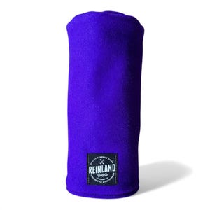 May include: A vibrant purple golf club head cover. The cover has a rectangular patch with the text "REINLAND Golf Co." and the words "QUALITY HANDMADE GOODS" and "TIMELESS STYLE & CRAFTSMANSHIP".