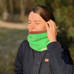 Puede incluir: Un calentador de cuello de forro polar verde y marr&oacute;n. El calentador de cuello es de color verde brillante con un forro interior marr&oacute;n. La persona de la imagen lleva una chaqueta azul oscuro.