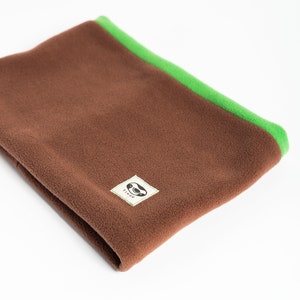 Puede incluir: Un calentador de cuello de forro polar marr&oacute;n con un ribete verde brillante. El calentador de cuello est&aacute; doblado y presenta una peque&ntilde;a etiqueta cuadrada con un logotipo. Dise&ntilde;ado para mantener el cuello caliente.