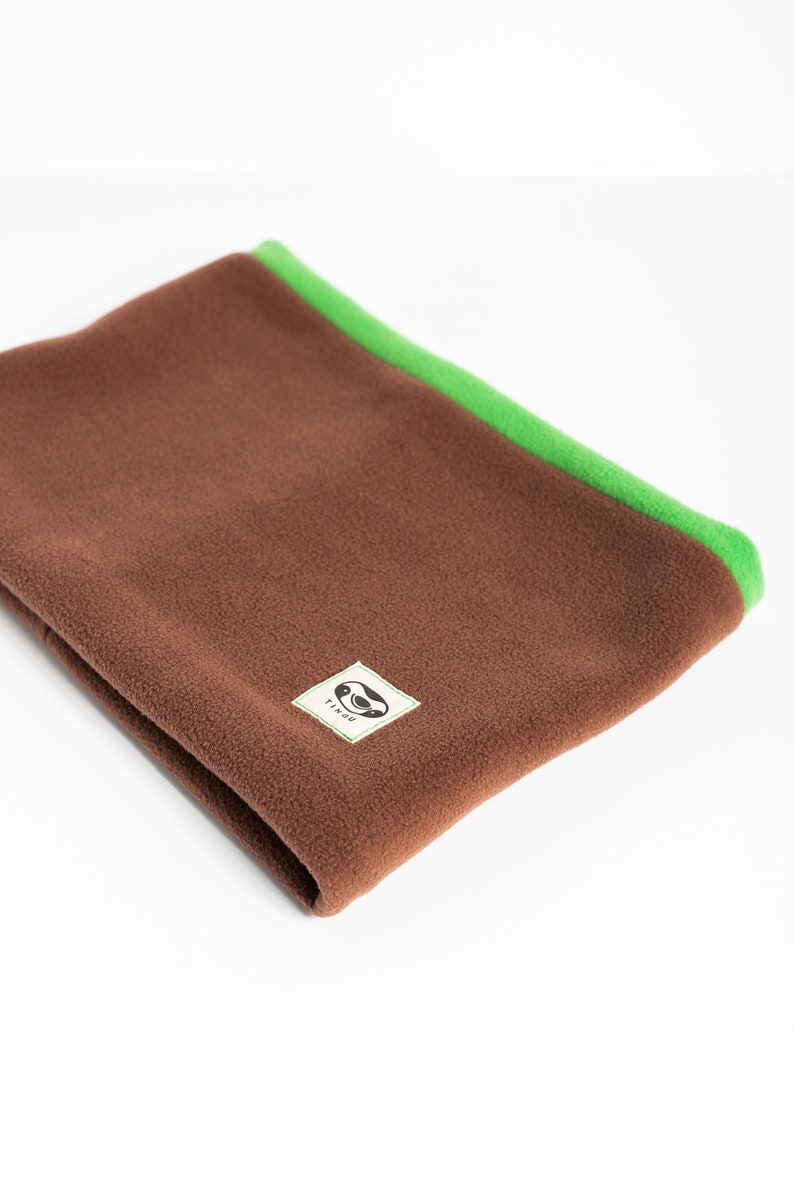 Puede incluir: Un calentador de cuello de forro polar marr&oacute;n con un ribete verde brillante. El calentador de cuello est&aacute; doblado y presenta una peque&ntilde;a etiqueta cuadrada con un logotipo. Dise&ntilde;ado para mantener el cuello caliente.