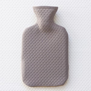 Puede incluir: Una botella de agua caliente gris con una superficie texturizada. La botella tiene un cuello estrecho y un cuerpo redondeado.