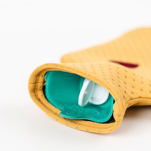 May include: A yellow hot water bottle with a teal blue rubber cover and a white plastic cap. The bottle is designed with small holes for heat distribution.