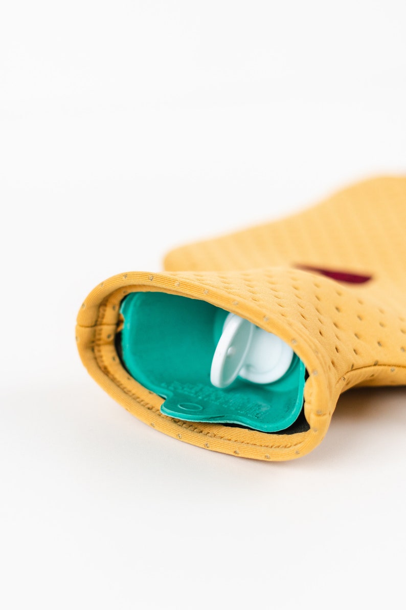 May include: A yellow hot water bottle with a teal blue rubber cover and a white plastic cap. The bottle is designed with small holes for heat distribution.