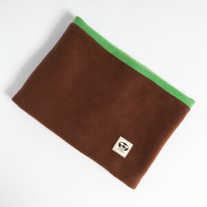 Puede incluir: Un calentador de cuello de forro polar marr&oacute;n con ribete verde. El calentador de cuello tiene una peque&ntilde;a etiqueta cuadrada con un logotipo. Este producto est&aacute; dise&ntilde;ado para mantener el cuello caliente en climas fr&iacute;os. El forro polar es suave y c&oacute;modo.