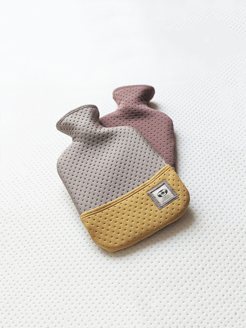 Puede incluir: Dos botellas de agua caliente con cubiertas de tela gris y amarilla. Las botellas son de goma y tienen una superficie texturizada. Las botellas est&aacute;n dise&ntilde;adas para ser usadas para la calidez y la comodidad.