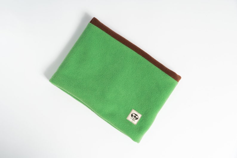 Puede incluir: Cuello de forro polar verde con ribete marr&oacute;n. El calentador de cuello tiene un peque&ntilde;o parche cuadrado con un gr&aacute;fico. Dise&ntilde;ado para mantener el cuello caliente en climas fr&iacute;os.