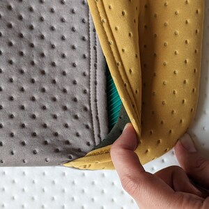 Puede incluir: Primer plano de una tela gris y amarilla con un patr&oacute;n texturizado. La tela est&aacute; doblada y muestra una capa verde y negra debajo.