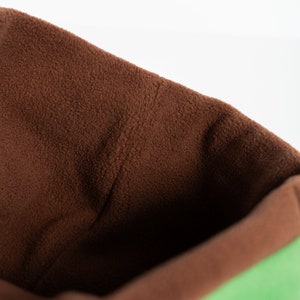 Puede incluir: Primer plano de un art&iacute;culo de tela suave verde y marr&oacute;n. El interior es de color marr&oacute;n intenso, mientras que el exterior es de un verde vibrante. El art&iacute;culo parece ser una bolsa o saco, con un tacto texturizado y afelpado.