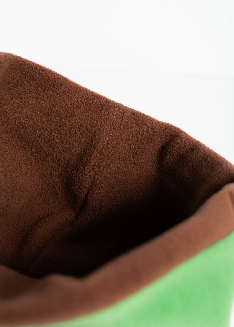 Puede incluir: Primer plano de un art&iacute;culo de tela suave verde y marr&oacute;n. El interior es de color marr&oacute;n intenso, mientras que el exterior es de un verde vibrante. El art&iacute;culo parece ser una bolsa o saco, con un tacto texturizado y afelpado.